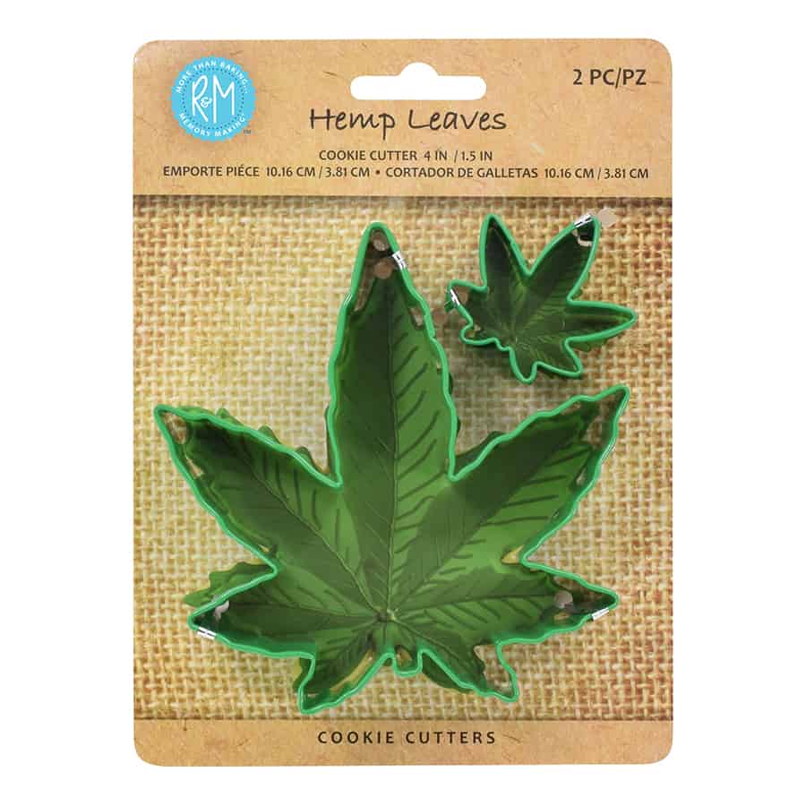 Two green marijuana weed leaf cookie cutters in large and small sizes displayed on kraft packaging over a tan burlap-textured background.