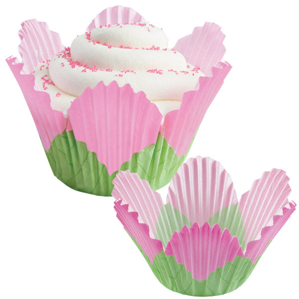 Pink and green petal-shaped baking cup holding a frosted cupcake with white swirled icing and pink sprinkles, shown beside an empty matching petal cup.