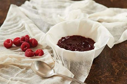 White bowl lined with a flour sack towel, filled with raspberry preserves, next to fresh raspberries and a spoon.